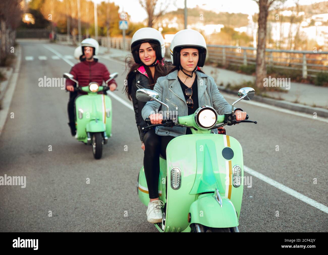 Green scooters with young people in motorcycle helmet driving in row on