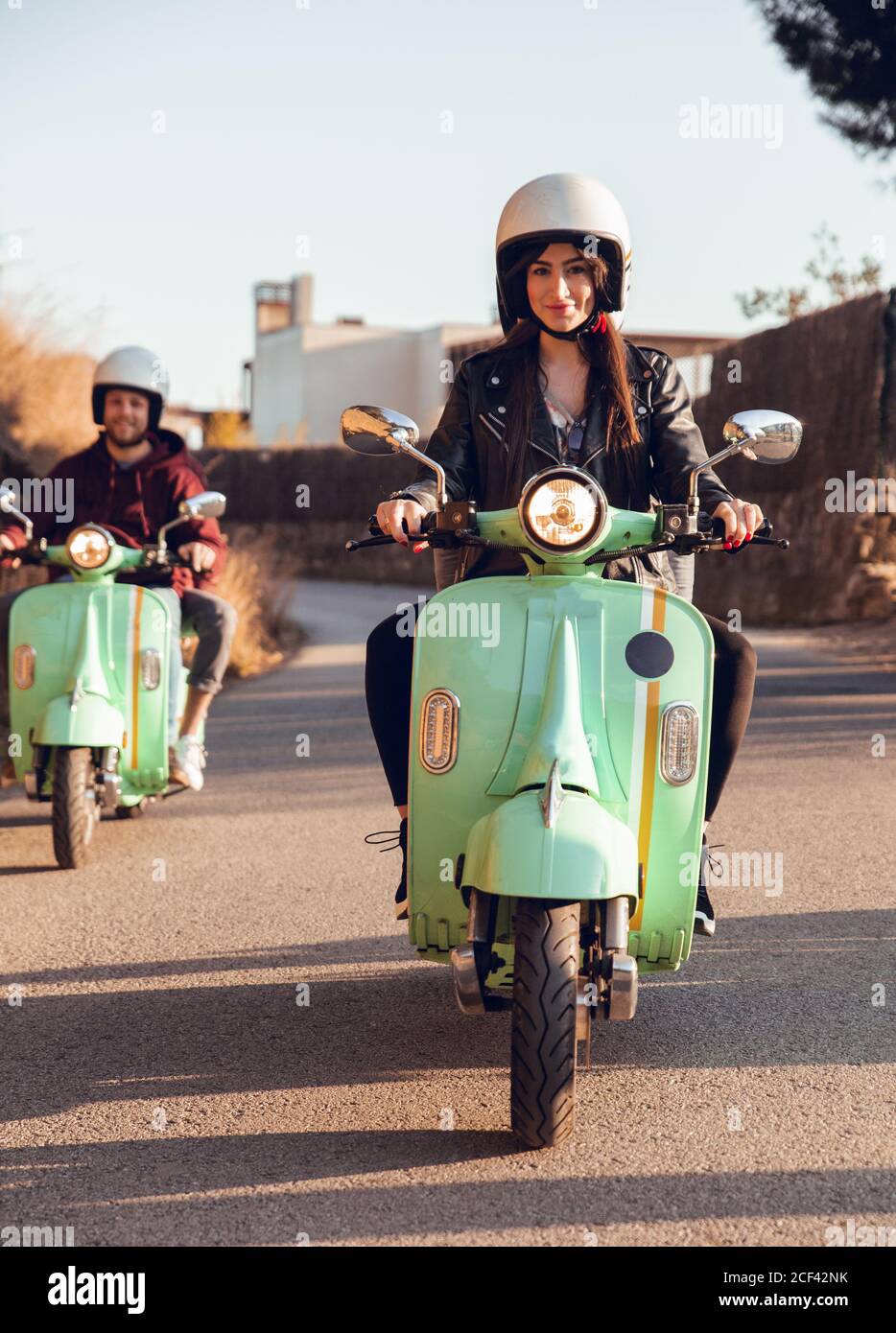 Green scooters with young people in motorcycle helmet driving in row on