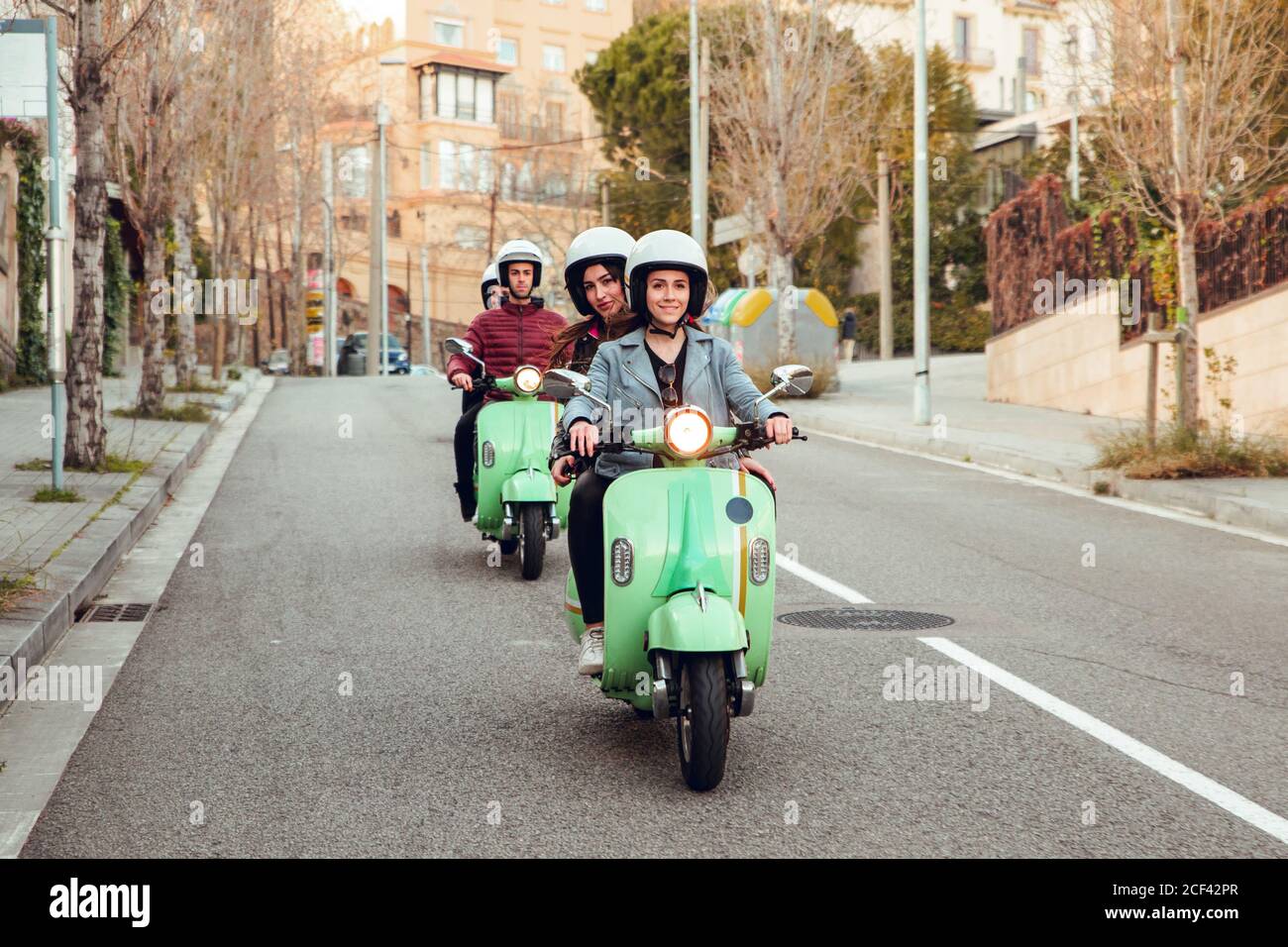 Green scooters with young people in motorcycle helmet driving in row on