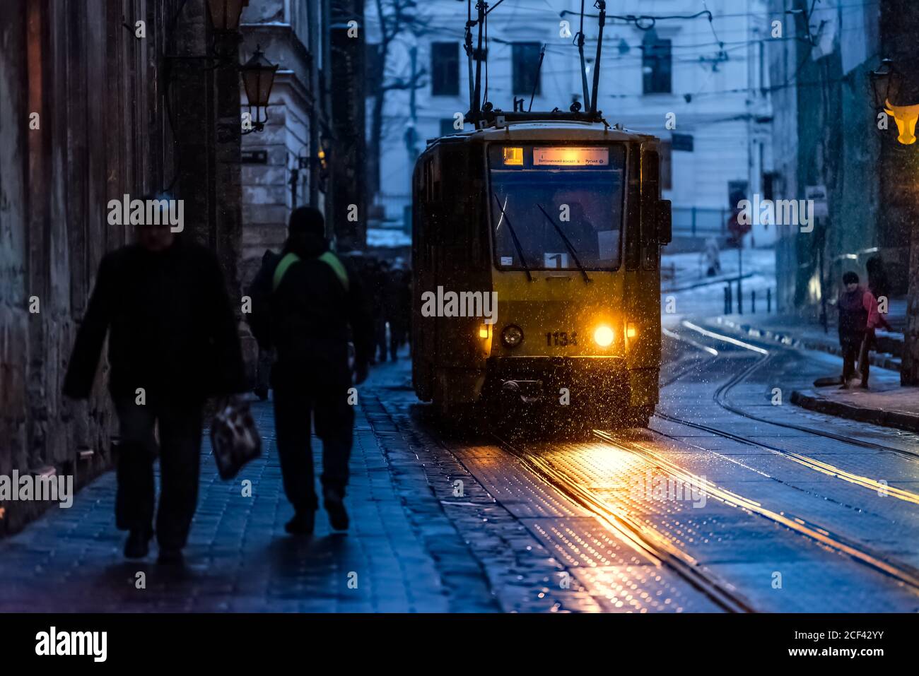 Lviv, Ukraine - December 28, 2019: Old town market square alley street in Lvov with winter snow at dark evening night and tram headlights illuminated Stock Photo