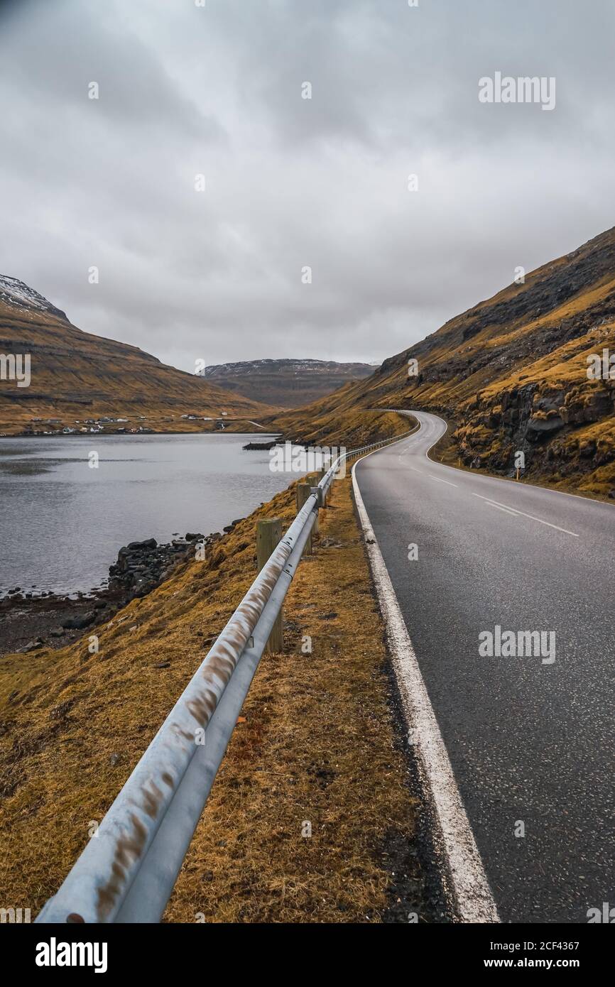Curvy asphalt road going through hilly terrain on cloudy day on Faroe Islands Stock Photo
