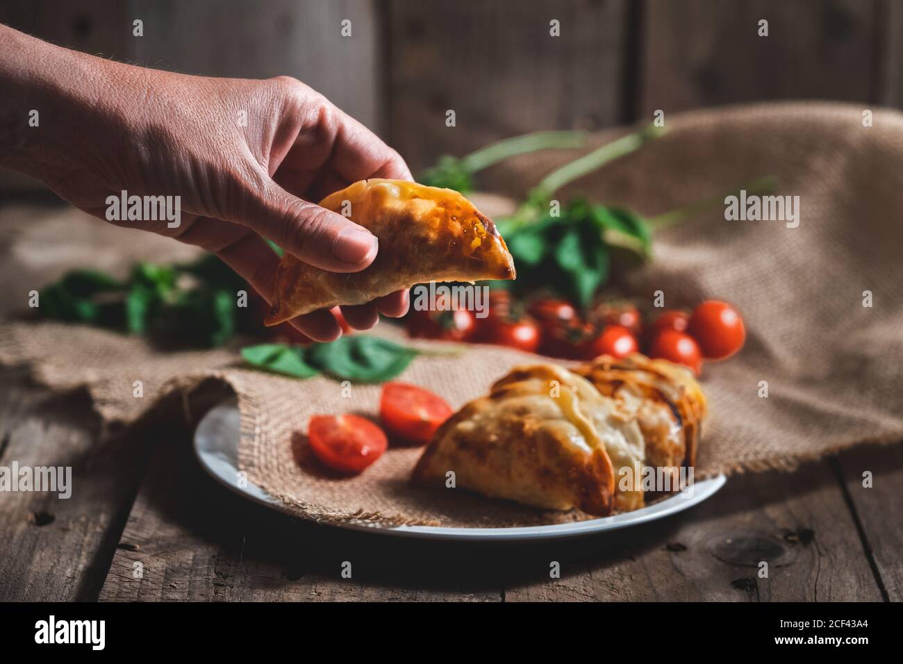 Unrecognizable Man Picking Up A Traditional Spanish Homemade Turnovers Served In Dish On Rustic Wooden Table With Fresh Spinach And Tomatoes Stock Photo Alamy