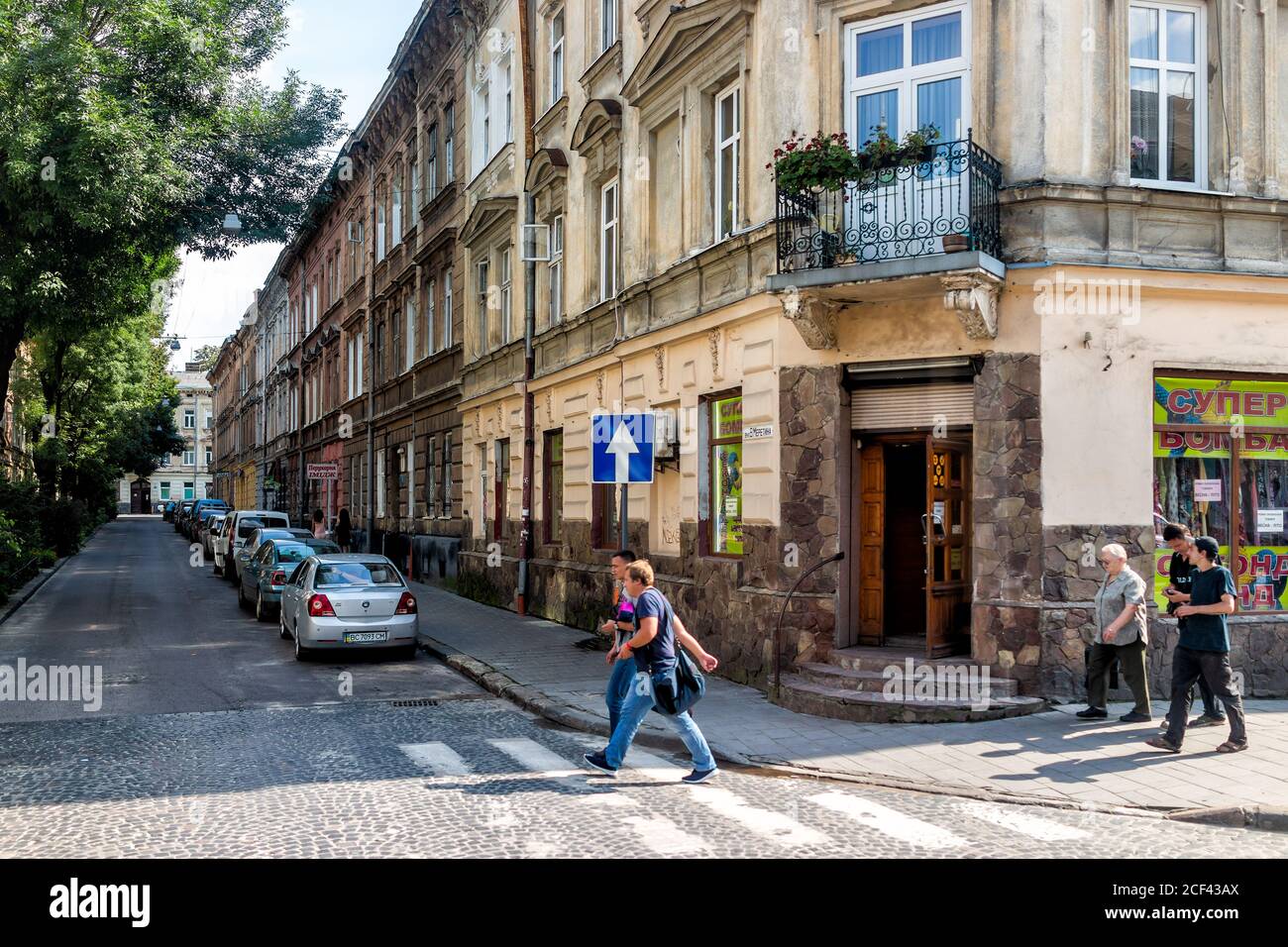 Lviv, Ukraine - August 1, 2018: Street in historic Ukrainian Lvov city during day with people crossing road by stores shops in old town and cobbleston Stock Photo