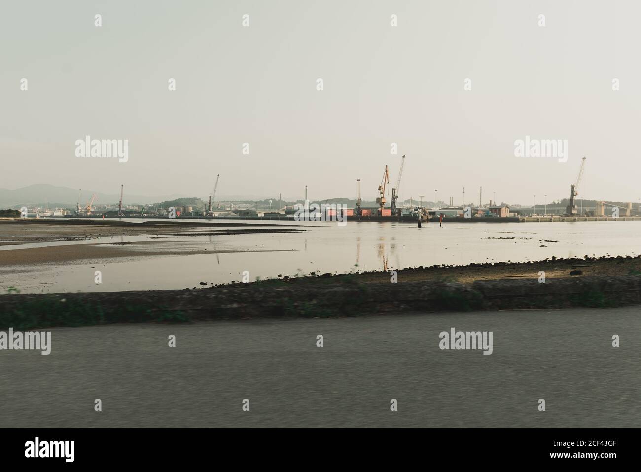 Industrial landscape with sea bay and port cranes in hilly terrain in cloudy day Stock Photo