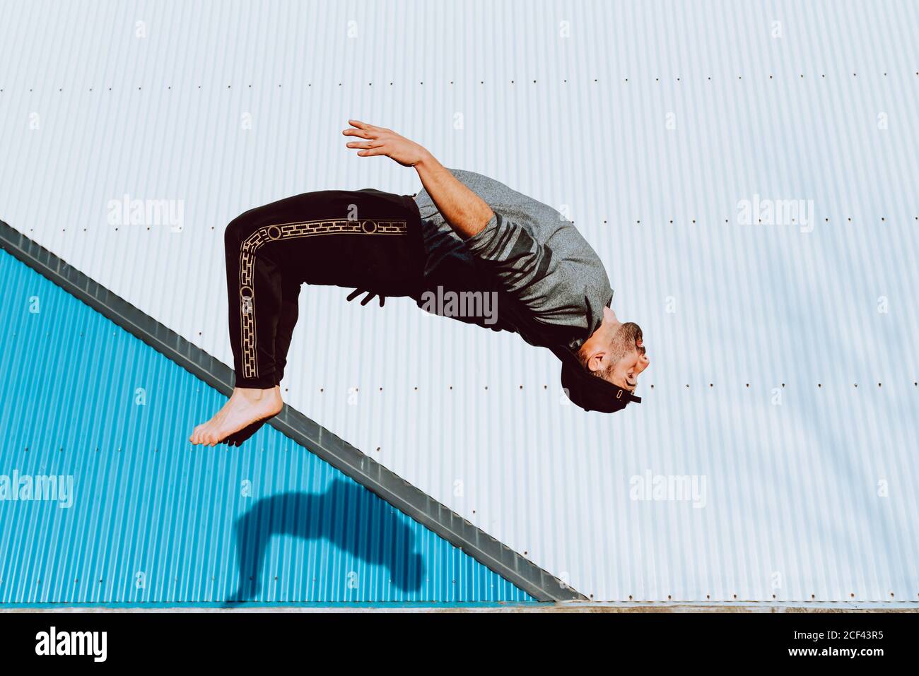 Side view of barefoot guy in stylish outfit performing flip near wall ...