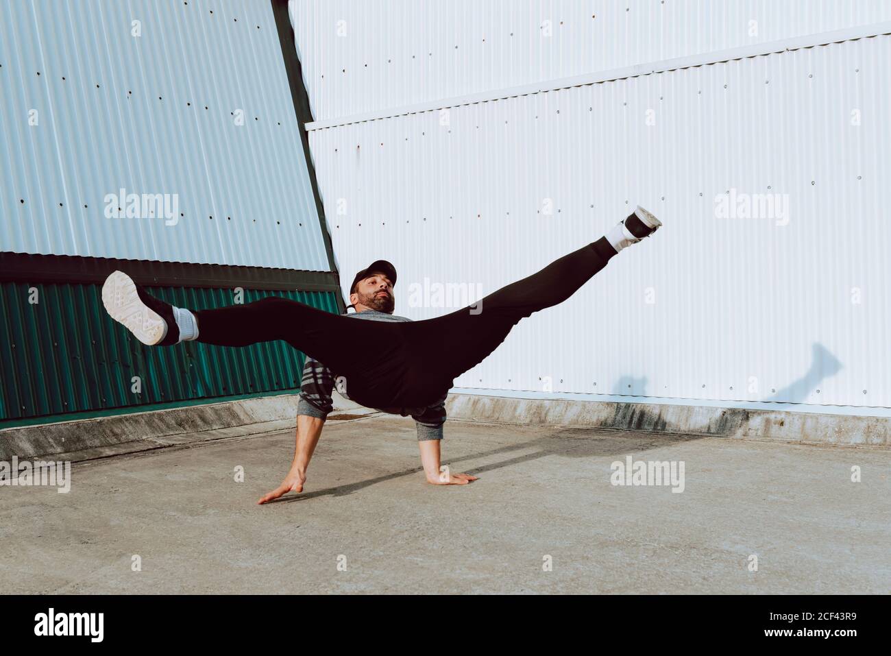Side view of barefoot guy in stylish outfit performing flip near wall ...