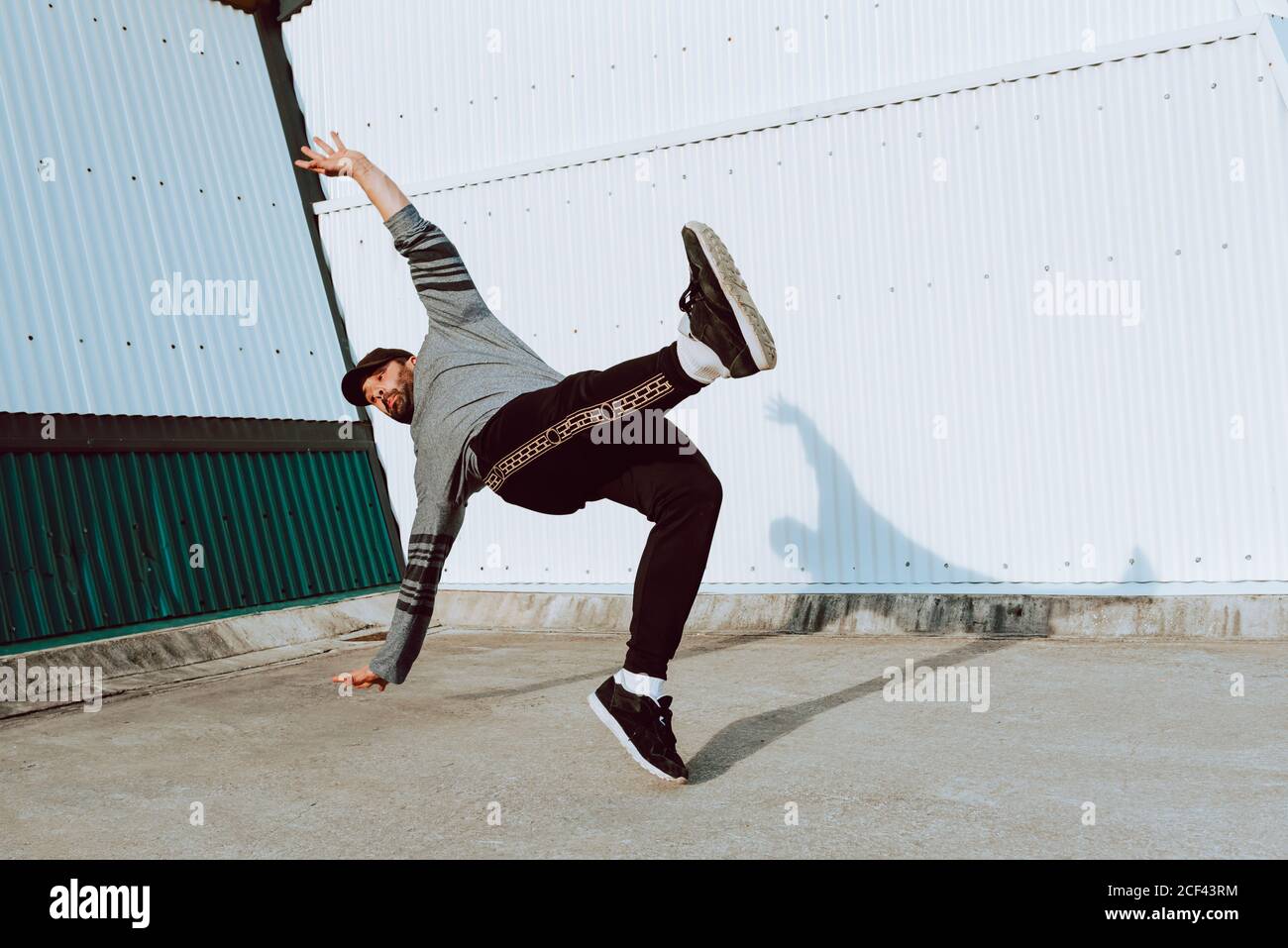 Side view of barefoot guy in stylish outfit performing flip near wall ...
