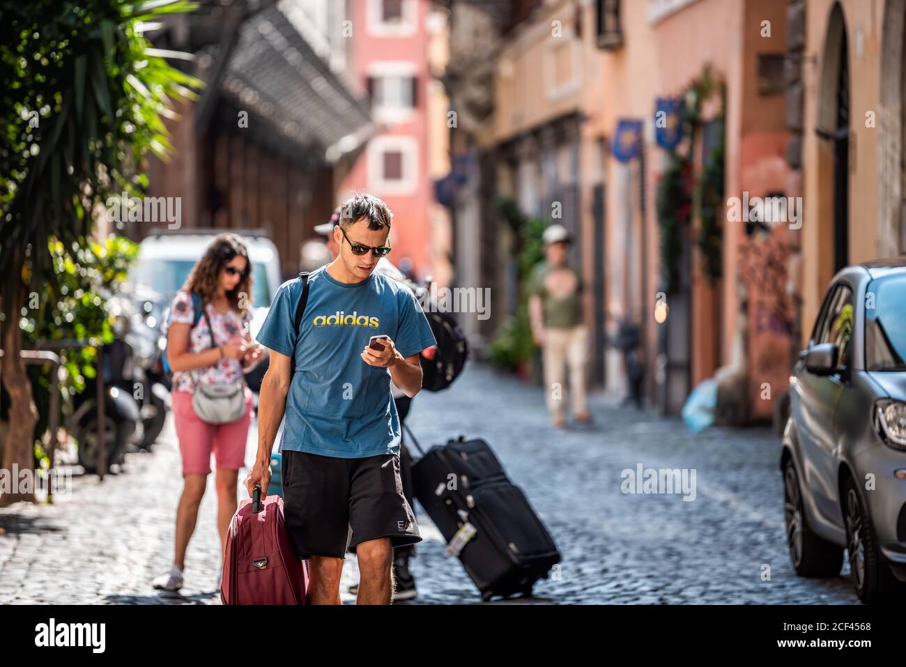 Rome, Italy - September 4, 2018: Narrow city town street with people family walking carrying luggage searching on phone for hotel Stock Photo