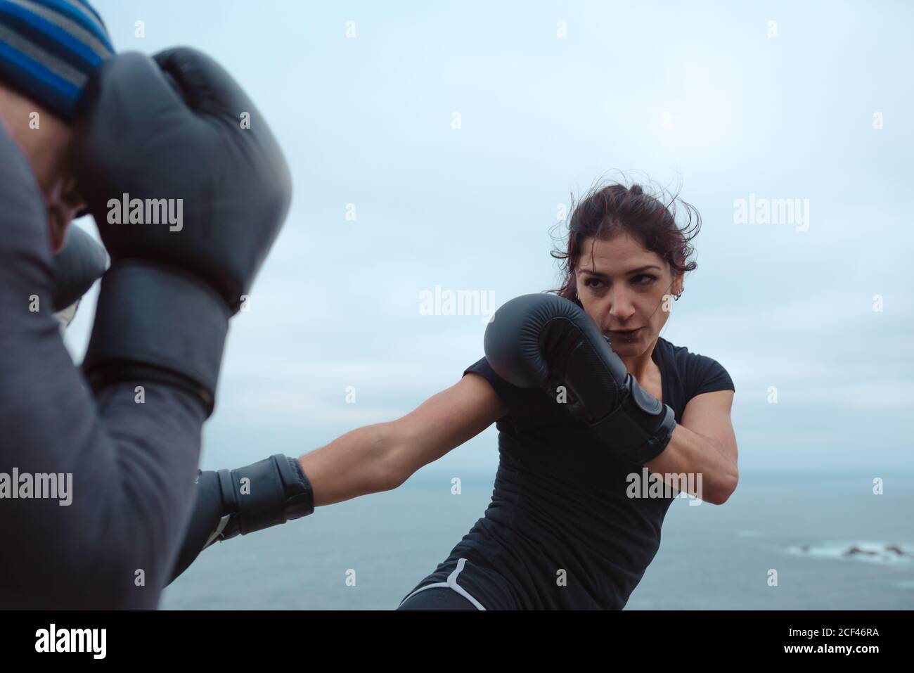 Side view of man and Woman in boxing gloves punching each other while standing on cliff against
