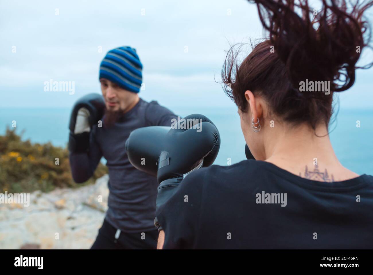 Side view of man and Woman in boxing gloves punching each other while standing on cliff against