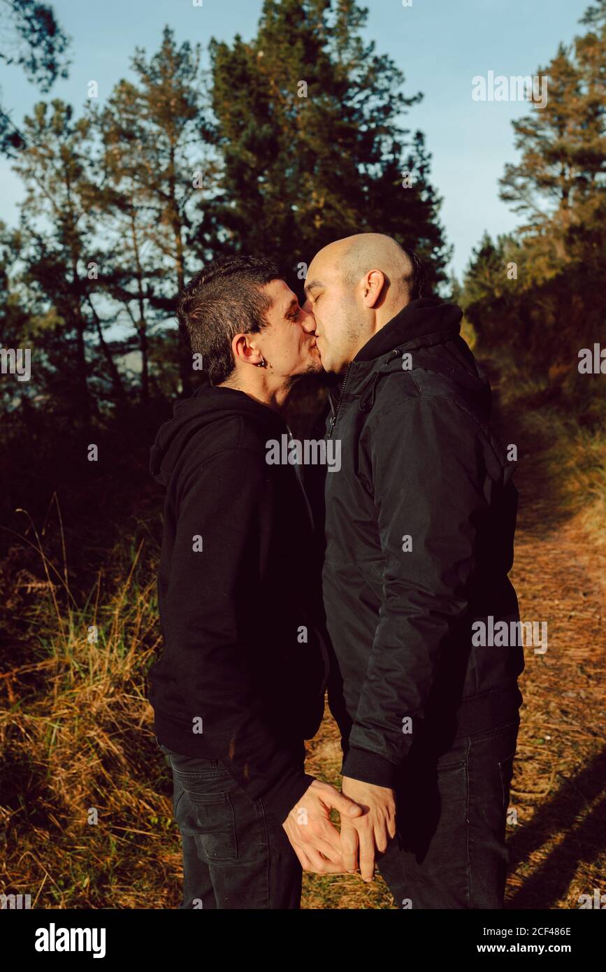 Side view of homosexual couple with closed eyes kissing on path in forest in sunny day Stock Photo