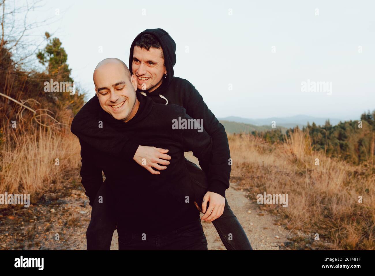 Happy homosexual couple having fun on route between plants on mountain and blue sky Stock Photo