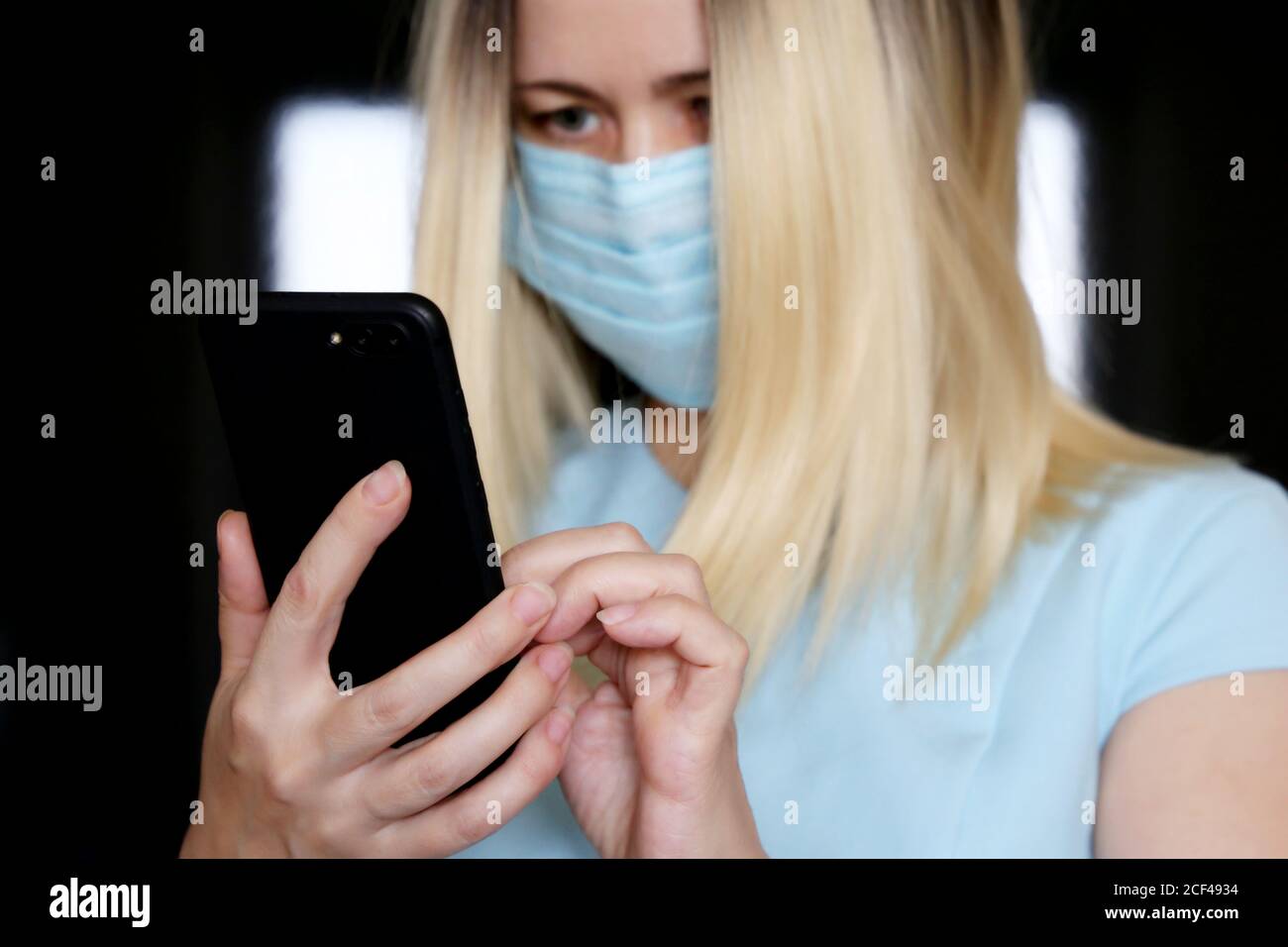 Blonde woman in face mask using smartphone, mobile phone in female hands closeup. Concept of safety work in office during coronavirus pandemic Stock Photo