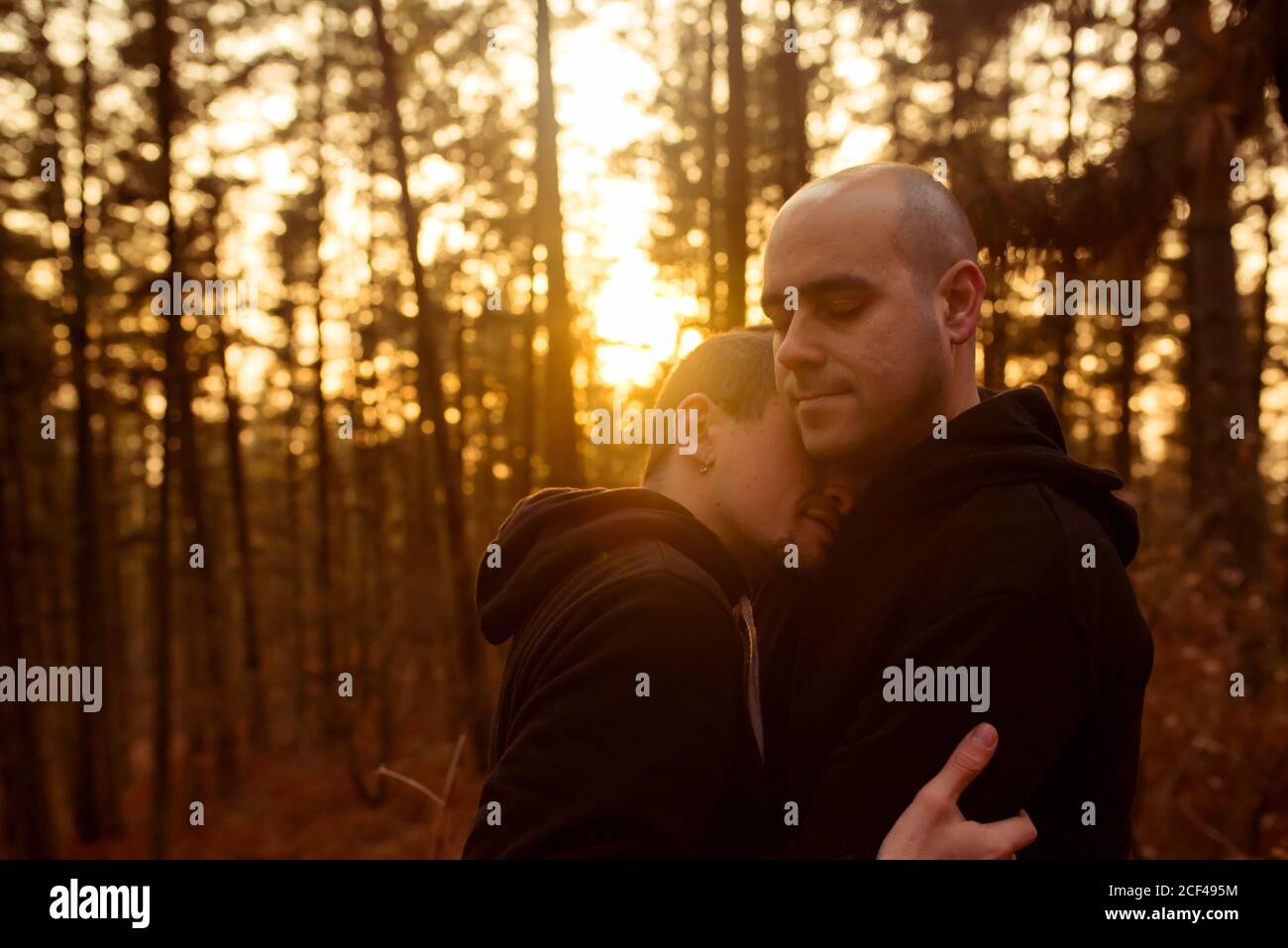 Side view of homosexual couple with closed eyes embracing in forest in evening Stock Photo