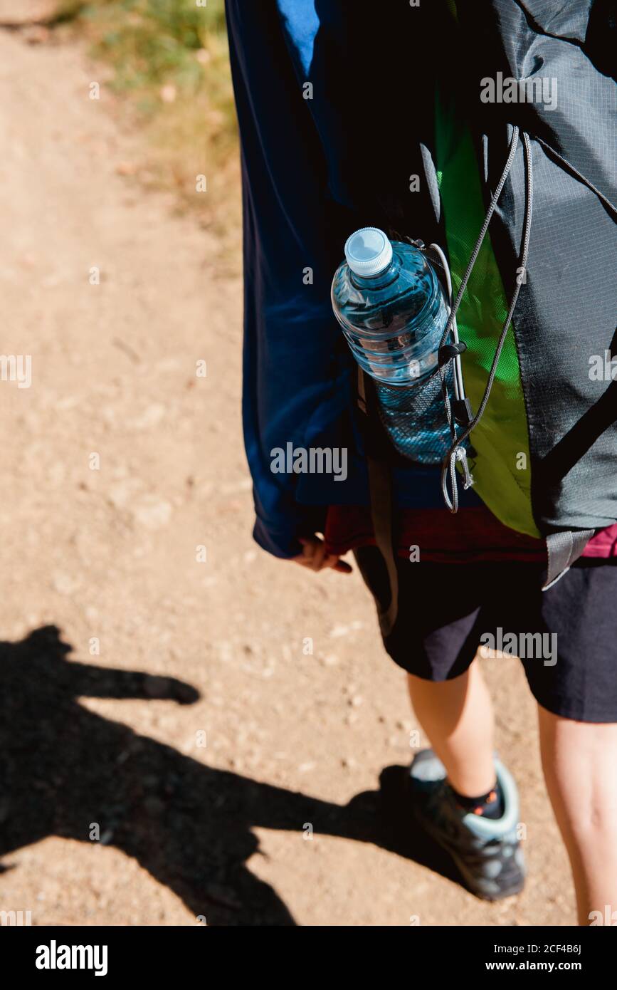 Back view of cropped anonymous female tourist with backpack having journey and walking on rural road through forest in summer Stock Photo