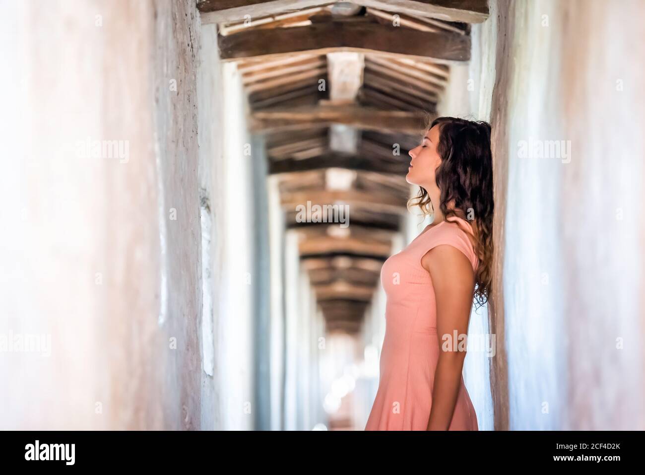 Young woman in light pink dress side profile standing leaning on wall of fortress tunnel passage in Castiglione del Lago in Italy Stock Photo