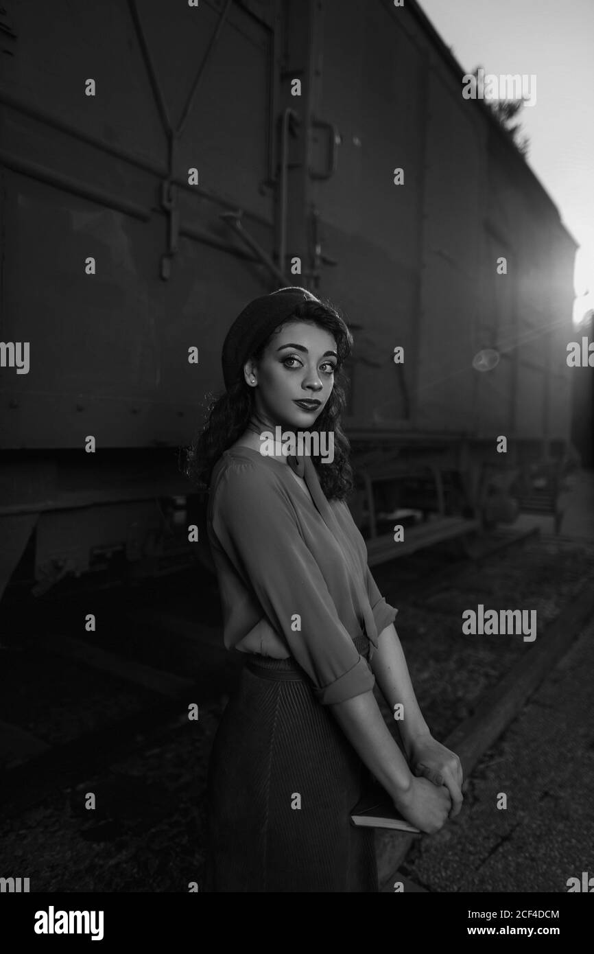 Dark haired female totally wearing clothes in vintage style standing near car train and holding open book in hands having dreaming look Stock Photo