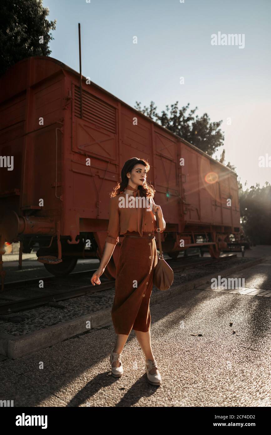 Dark haired female totally wearing terracotta clothes in vintage style standing near terracotta car train and holding open book in hands having dreaming look Stock Photo