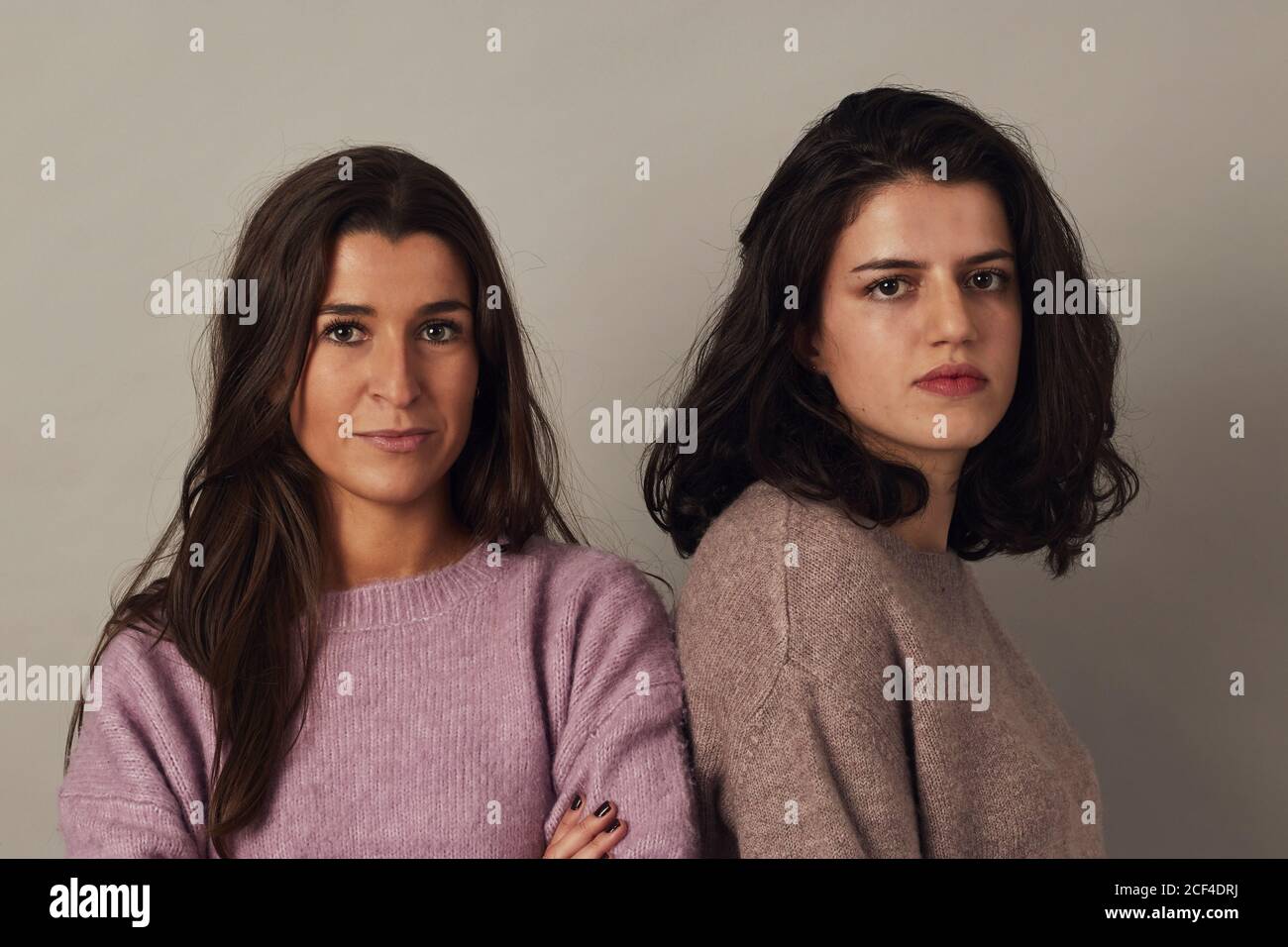 Satisfied young charming dark haired women wearing sweaters and looking at camera while standing together on gray background in studio Stock Photo
