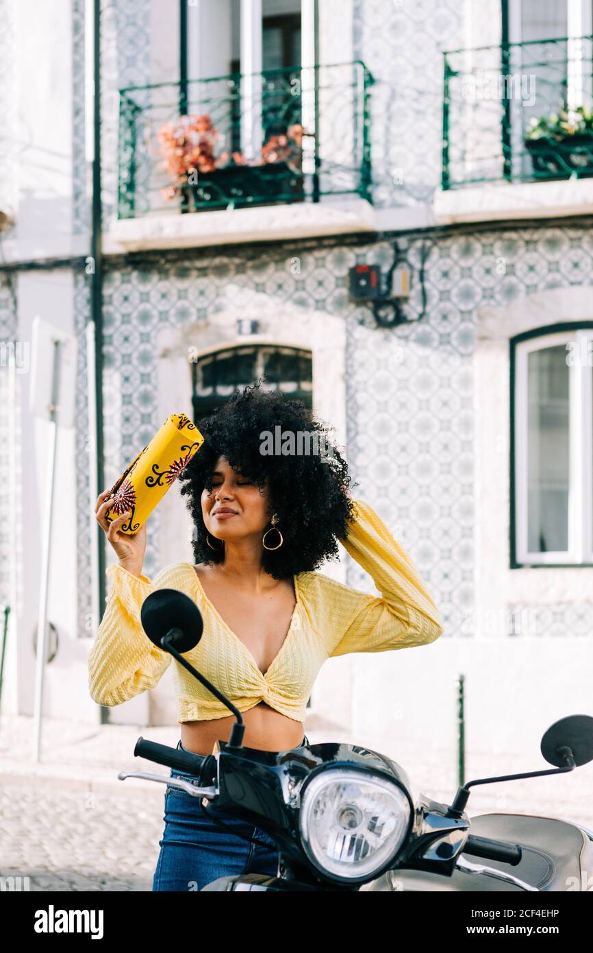 Young African American Woman with black curly hair sitting on motorcycle and closed eyes with bag on hand Stock Photo