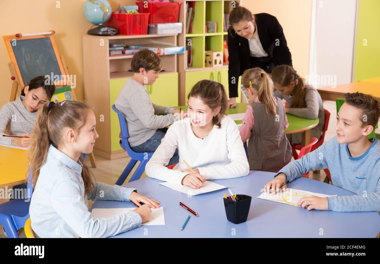 Pupil elementary age drawing at class, female teacher helping Stock ...