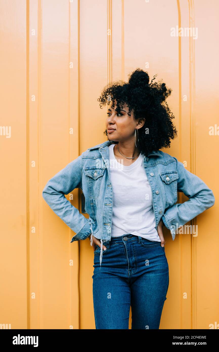 Young African American Woman in jeans and denim jacket leaning on yellow  door and looking away Stock Photo - Alamy