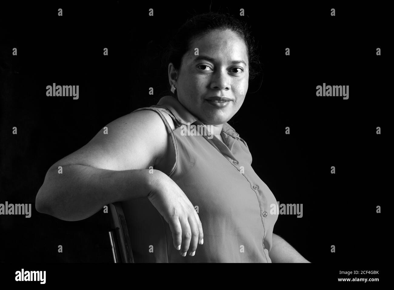portrait of a latin woman sitting on chair and looking at camera on black background, black and white Stock Photo