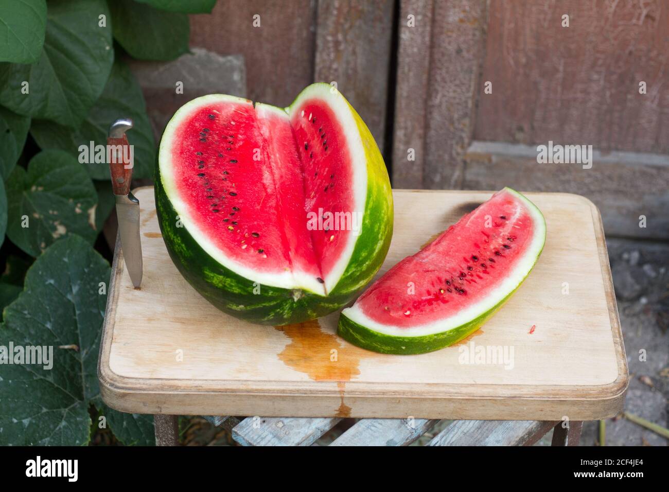 Fresh red watermelon on wooden cutting board near old door to village house, picnic concept, selective focus Stock Photo