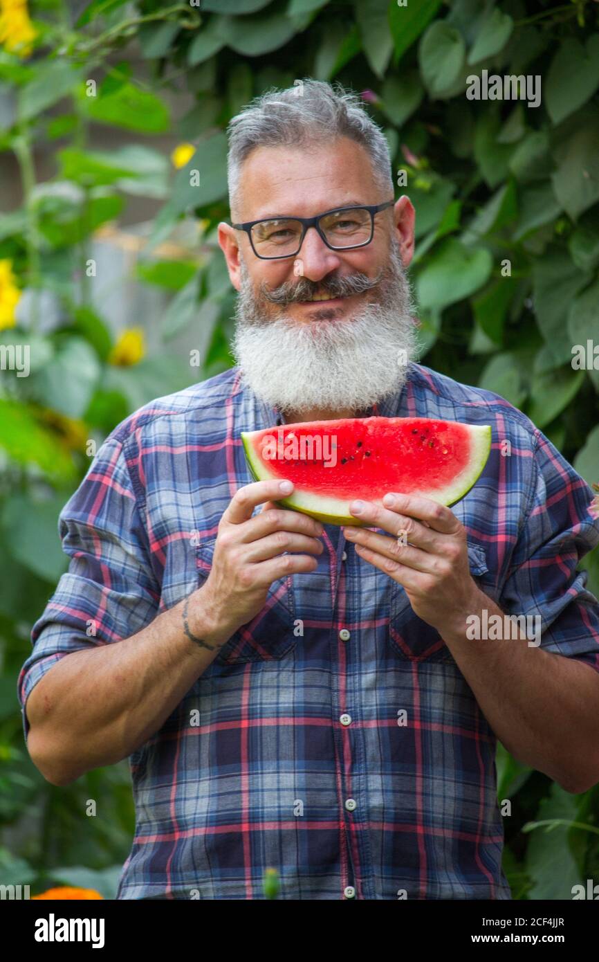 Portrait of mature bearded male farmer with ripe watermelon, own harvest concept, selective focus Stock Photo