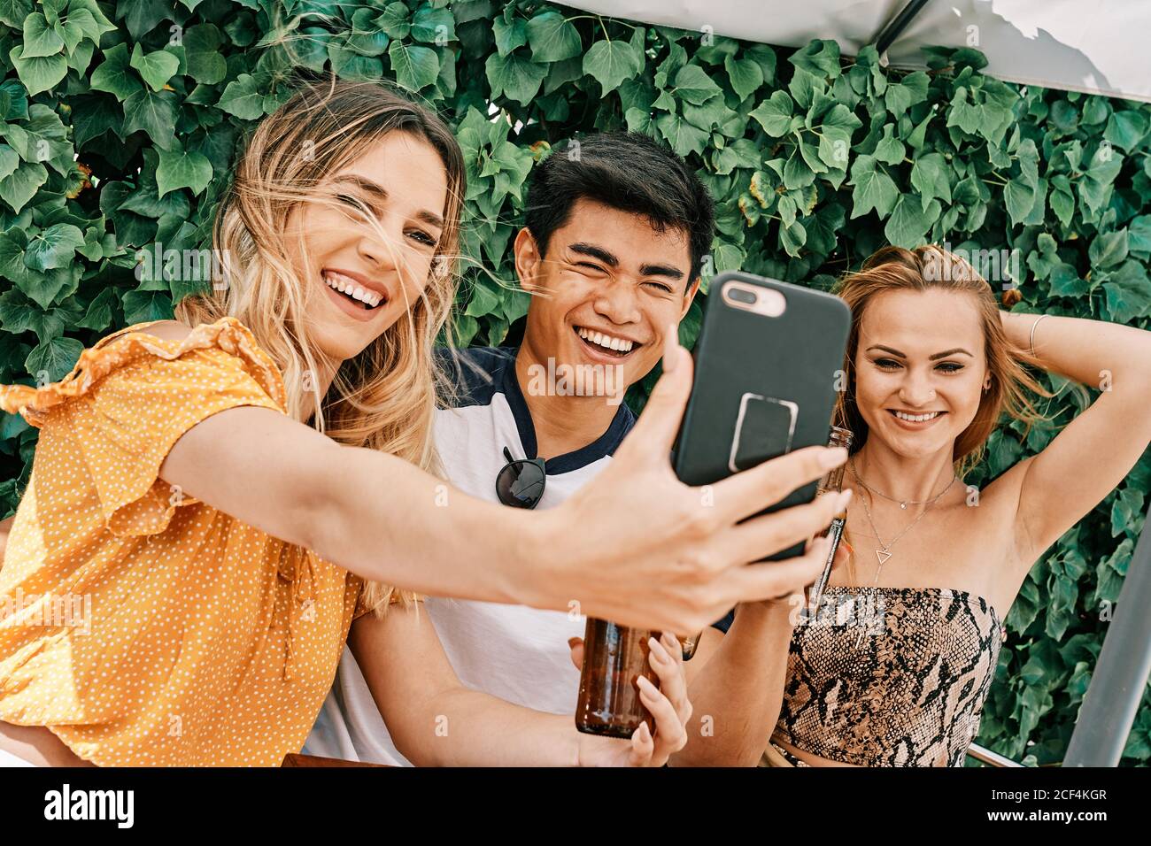 two women and a man drinking beer and taking selfies Stock Photo