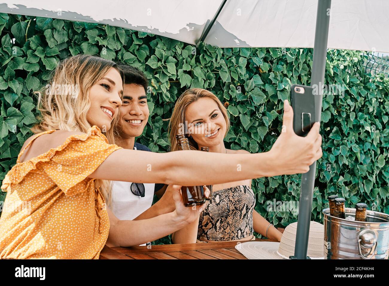 two women and a man drinking beer and taking selfies Stock Photo