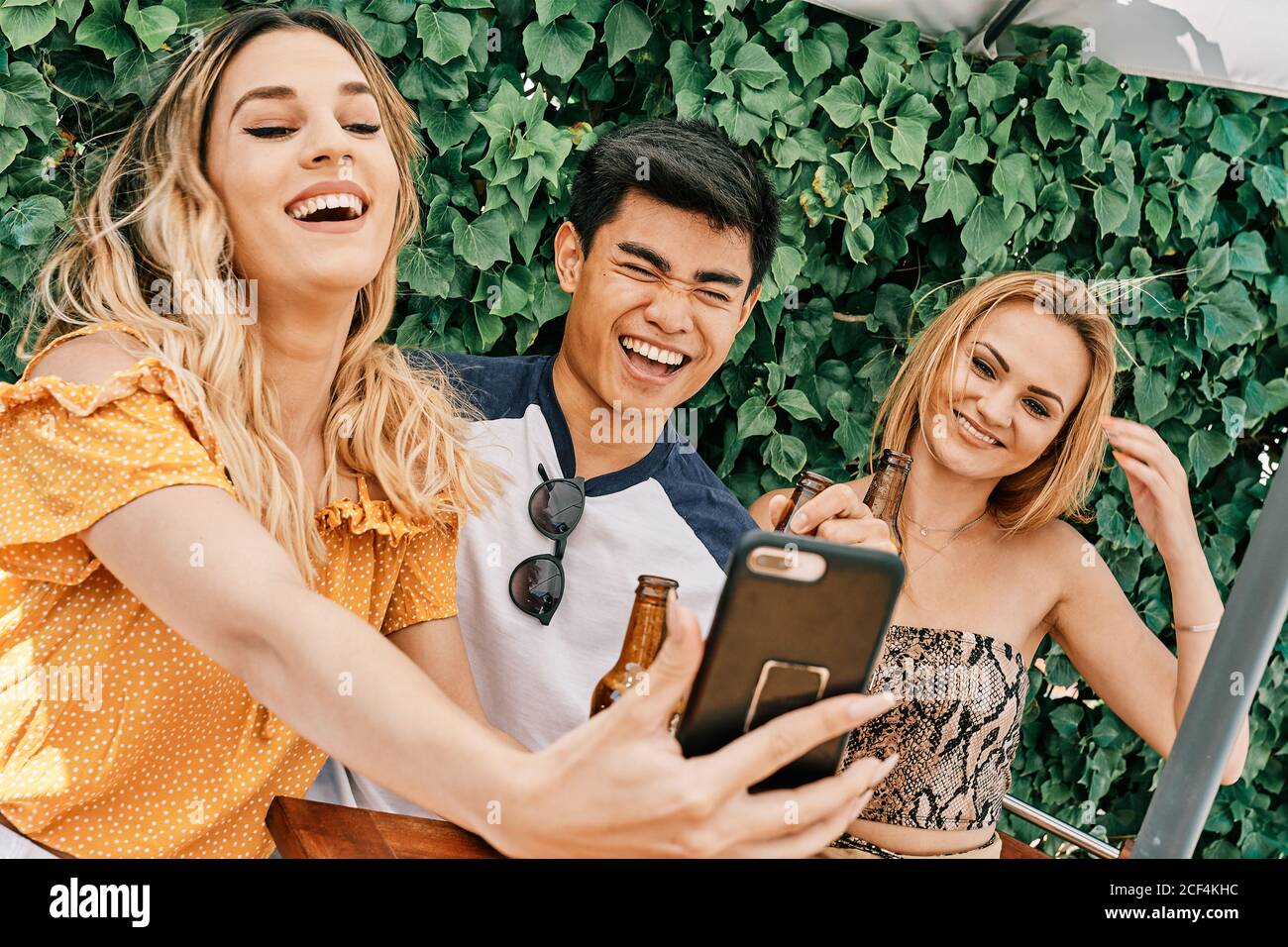 two women and a man drinking beer and taking selfies Stock Photo