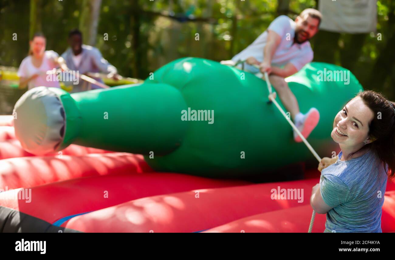 Laughing young woman pulling rope of inflatable rodeo bottle, trying to ...