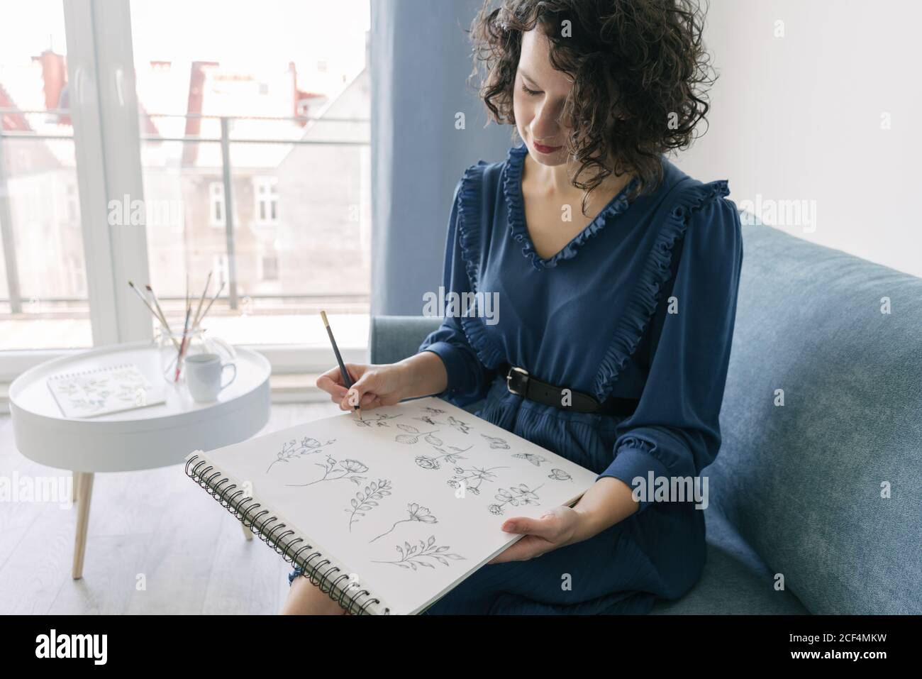 Elegant Woman sitting on a sofa drawing on a notebook at home Stock Photo