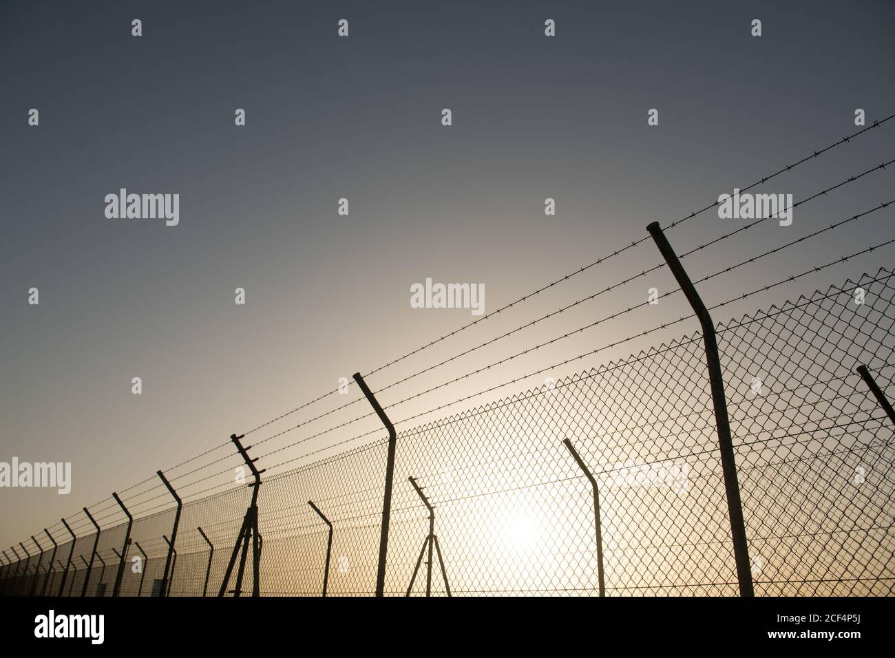 Metal security fence located in front of cloudless sky with bright sun ...