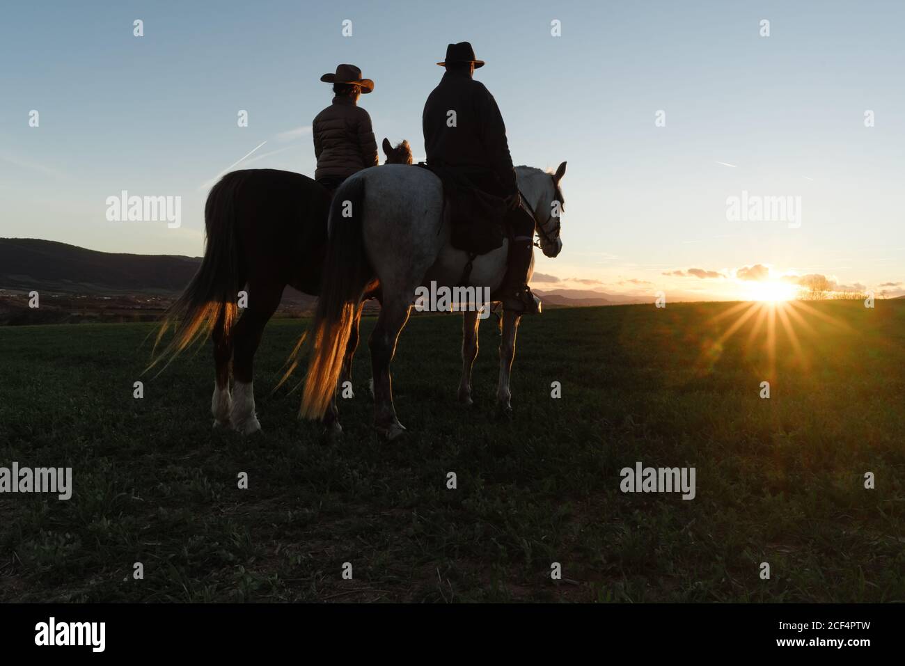 man and Woman riding horses against sunset sky on ranch Stock Photo