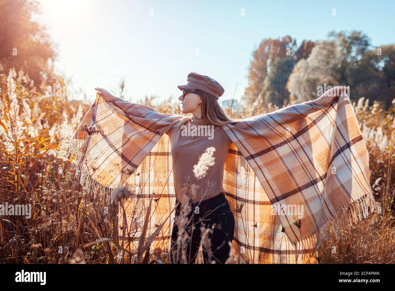 Autumn fashion. Young woman wearing stylish poncho, cap outdoors raising hands. Clothing and accessories. Stock Photo