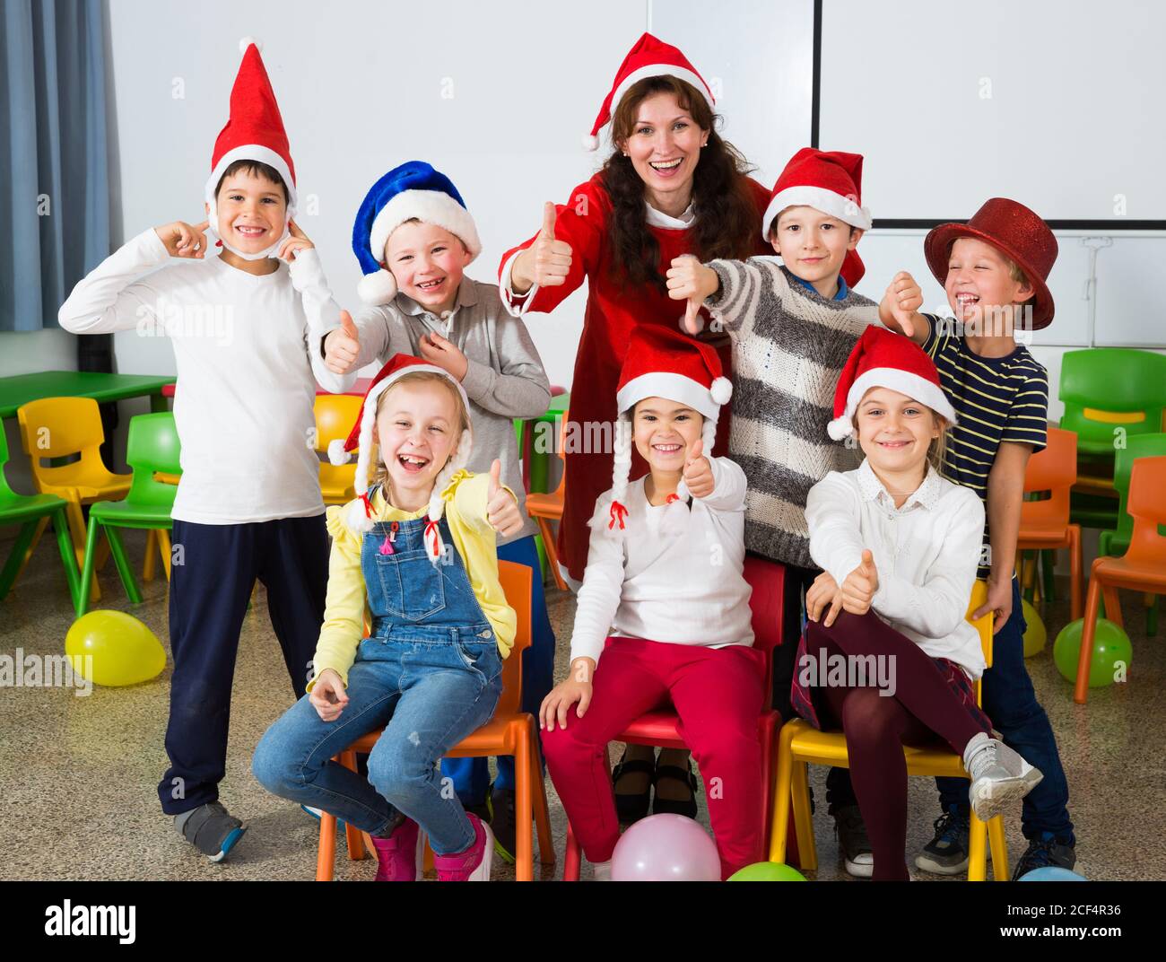 Cheerful group of pupils with female teacher wearing Santa hats posing ...