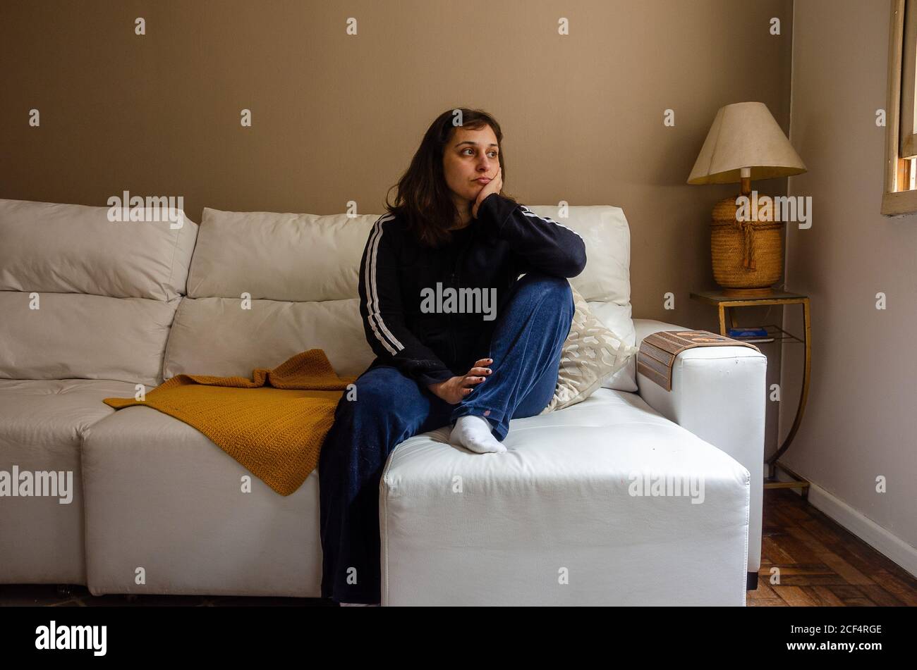 young latin woman sitting on a white couch looking contemplative Stock Photo