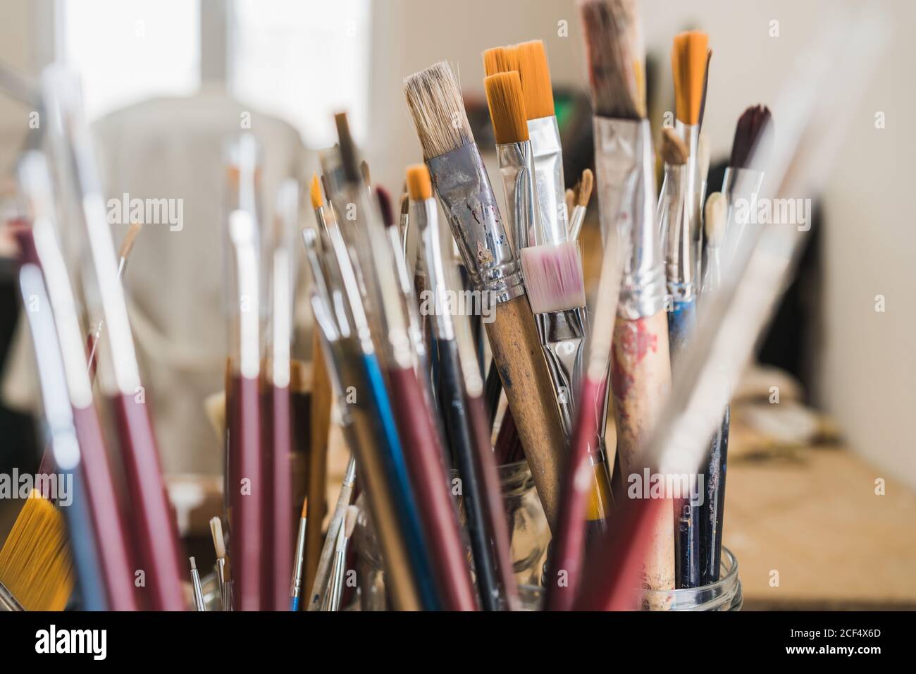 Set of various multi colored artists paintbrushes locating in glass on wooden table of modern art workshop on sunny day Stock Photo