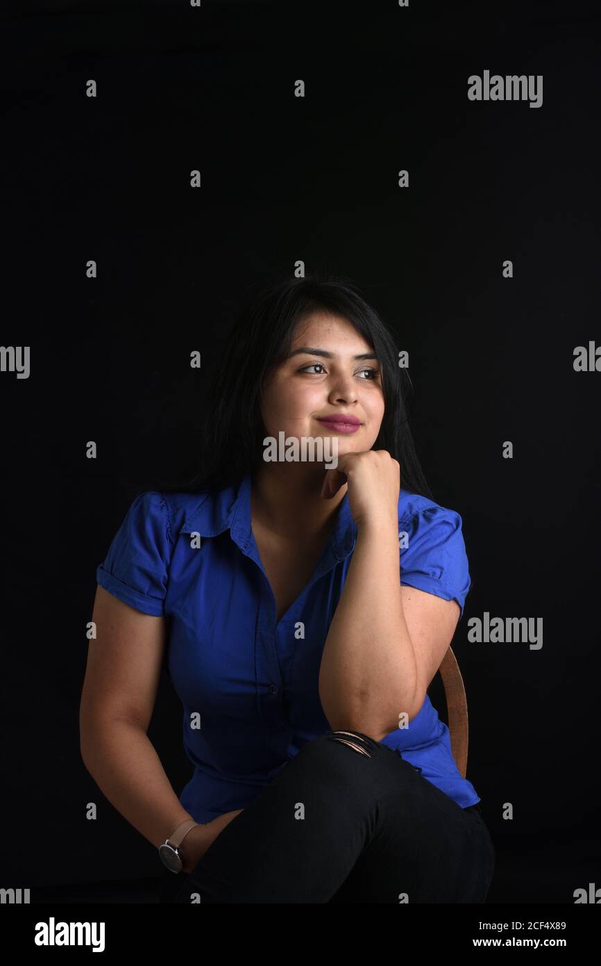 portrait of a latin woman sitting on chair and look side on black background, Stock Photo