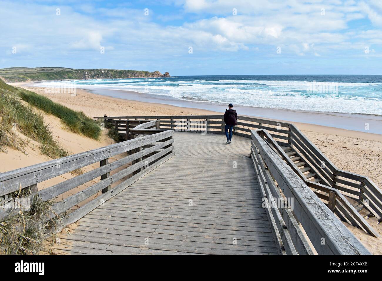 A visitor walks along the boardwalk down to the Cape Woolamai Surf Beach on Phillip Island, Australia.  Golden sand and blue water of Bass Strait. Stock Photo