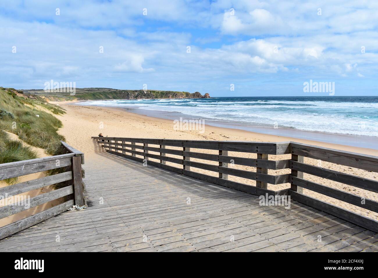 A wooden boardwalk leads down to the deserted Cape Woolamai Surf Beach in Phillip Island Nature Park.  Waves breaking on the golden sand beach. Stock Photo
