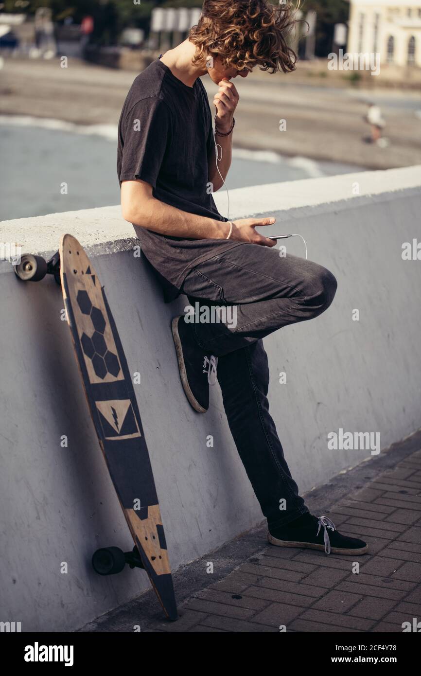 cute man longboarder taking break after boarding outside at sea background Stock Photo