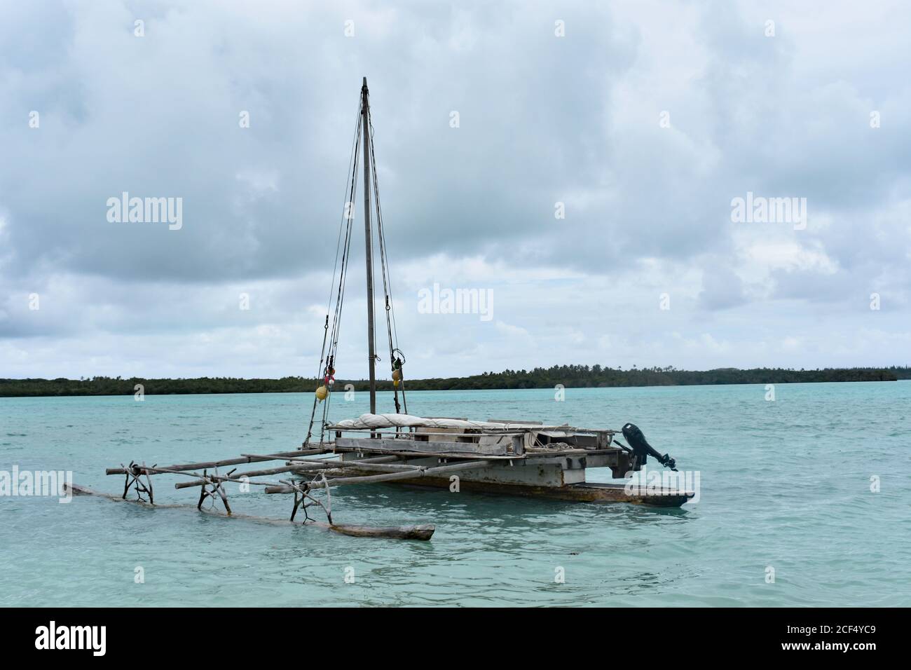 A small local fishing boat anchored in light blue tropical waters off of Vao Beach on Isle Of Pines, New Caledonia on an overcast cloudy day. Stock Photo