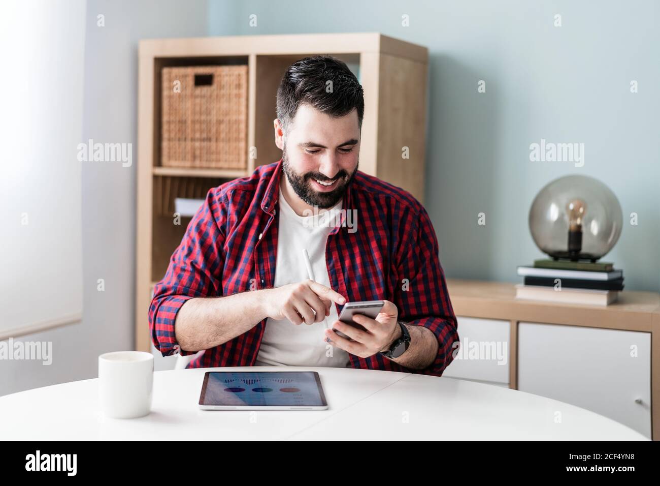 A young man is typing on the mobile phone. The man is working from home. The entrepreneur is using his phone and smiling Stock Photo