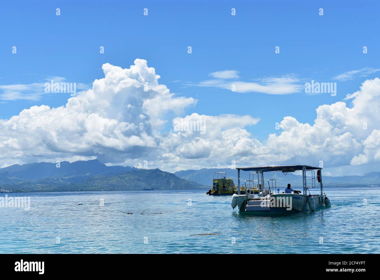 Two small boats off the coast of South Sea Island.  The mountains of Viti Levu can be seen across blue waters of Nadi Bay. Fiji, South Pacific. Stock Photo