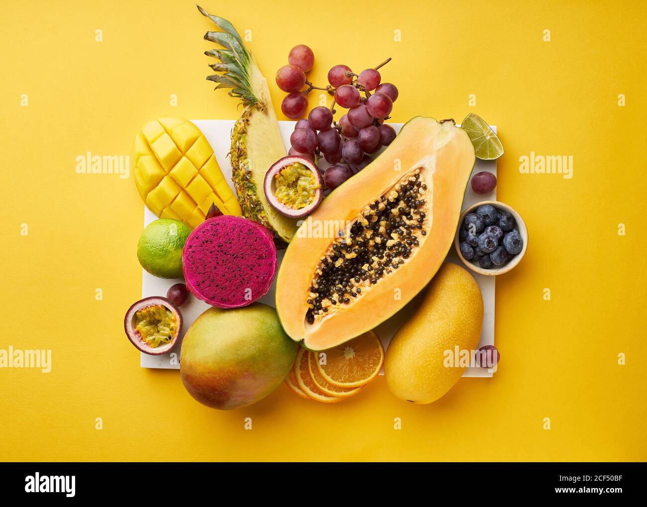 Top view of flat lay with tropical fruits on a tray: papaya, mango, dragon fruit and pineapple on yellow background. Summer treat Stock Photo