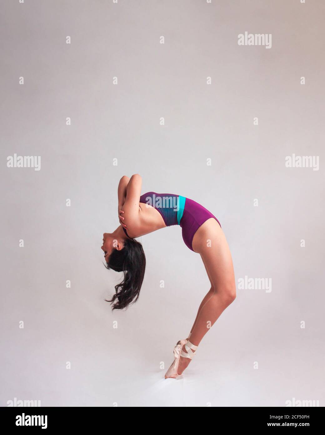 Side view of graceful woMan in leotard and pointe shoes bending back while dancing against gray background Stock Photo