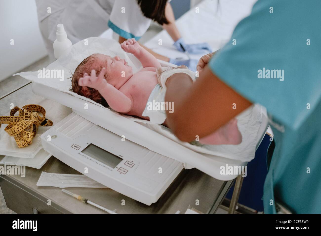 From above side view of crop medical specialist weighting newborn baby on scale in modern hospital Stock Photo